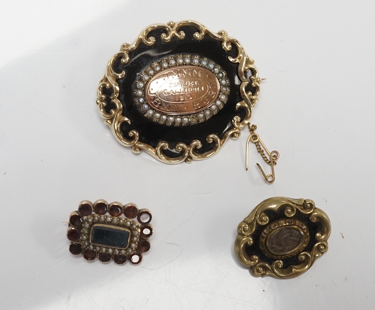 Three assorted late 19th/early 20th century yellow metal mounted mourning brooches, including black enamel and split pearl inscribed 'JMMM. BJBW. JBMW. 23rd Oct Gallipoli 1915', 45mm and a garnet and split pearl. Conditi